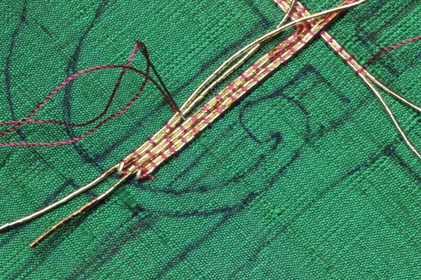 The needle goes down between threads and angles toward previous rows