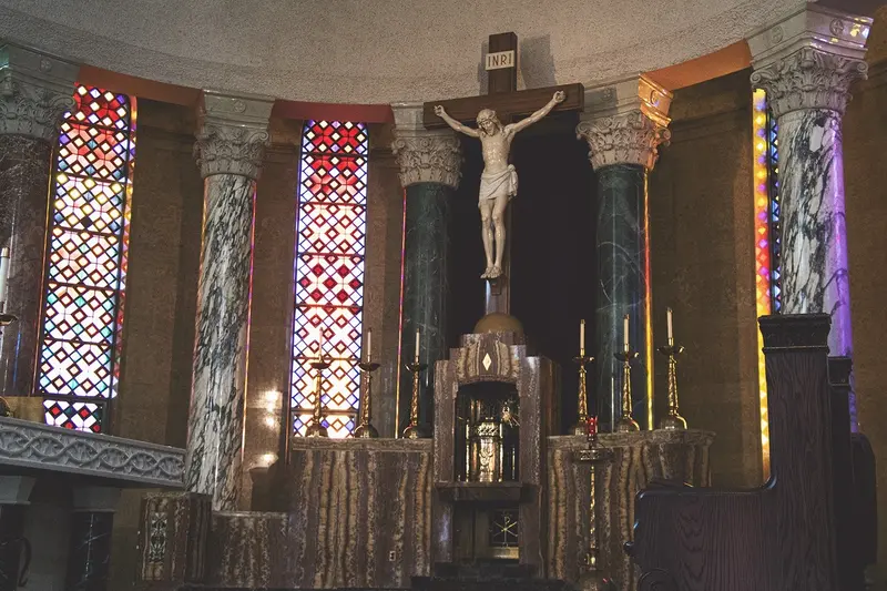 Interior of a church featuring a crucifix above the altar, with marble columns and stained glass windows